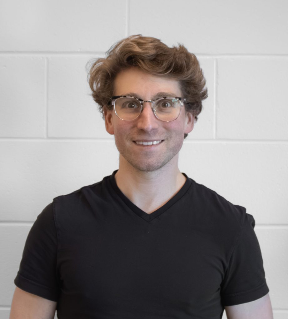Smiling man with glasses in front of a white wall