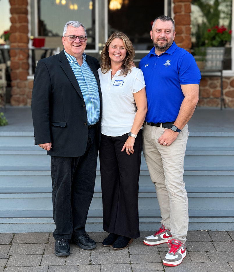 Three smiling people pose in front of a stone building.
