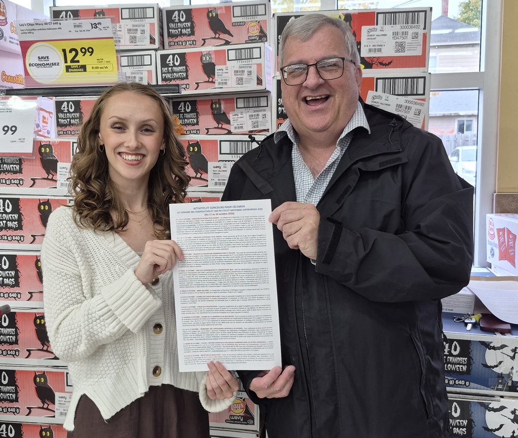 Two people present a document in front of Halloween boxes.