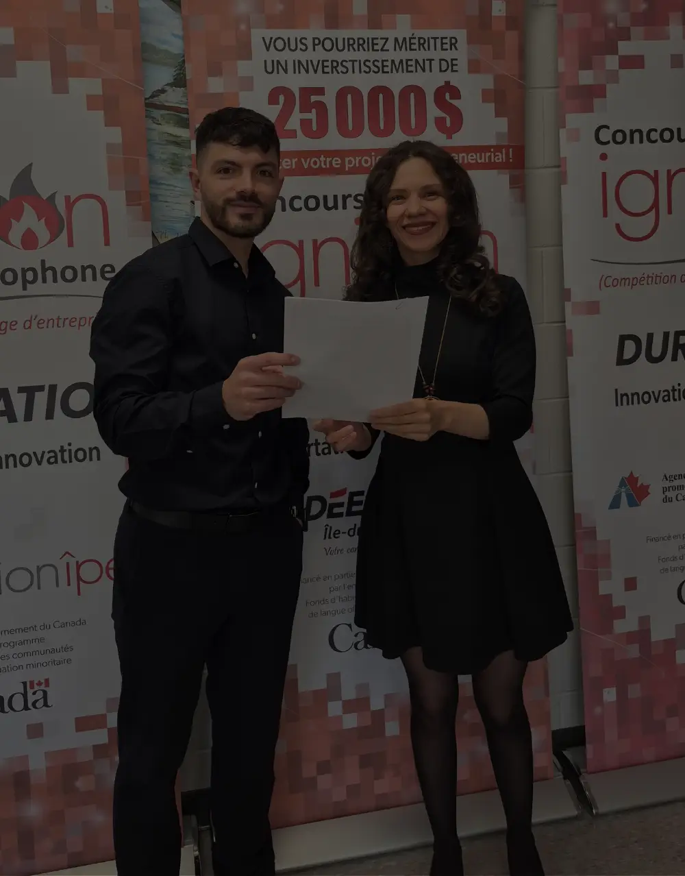 Two participants present a document in front of contest banners.